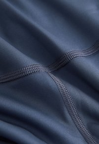 Gros plan d’un tissu bleu foncé avec des coutures doubles détaillées créant des lignes croisées sur un matériau lisse légèrement plié.