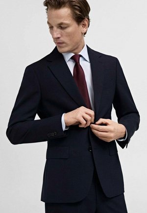 Navy, tailored suit with a notched lapel, single-breasted design, and two front pockets. Worn over a light blue shirt and burgundy tie.