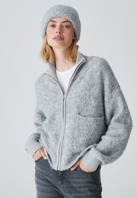 Light gray zip-up fleece jacket with a high collar, textured surface, and ribbed cuffs, paired with a matching textured beanie.