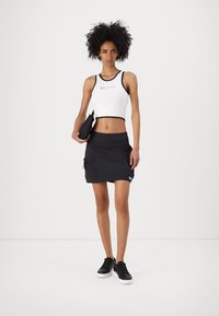 Fehér crop top fekete díszítéssel, szöveges részlettel; fekete szoknya oldalsó zsebekkel, sima felszíntel; fekete sportcipők fehér talppal.