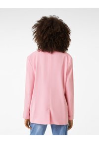 Pink blazer with a relaxed fit, smooth texture, long sleeves, back vent detail, and subtle seams. Worn over blue jeans.