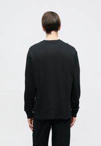 Μαύρο πουκάμισο με μακριά μανίκια φτιαγμένο από λείο ύφασμα, με στρογγυλή λαιμόκοψη και χαλαρή εφαρμογή. Ραμμένα μανίκια και στρίφωμα, χωρίς ορατά σχέδια ή γραφικά.