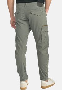 Olijfgroene cargo-broeken, met meerdere zakken, ritsaccenten en een taps toelopende pasvorm. Gemaakt van lichtgewicht stof met een zachte textuur.