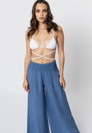 Top bikini bianco a triangolo con bretelle incrociate abbinato a pantaloni larghi in lino blu con elastico in vita e gambe ampie.