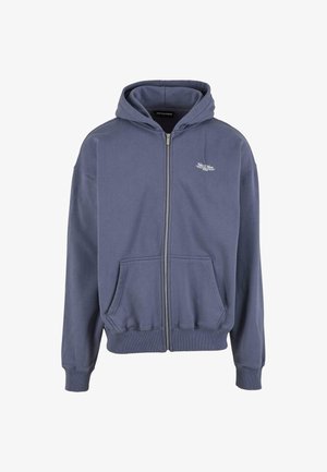 Tmavě modrá zipová mikina s kapucí. Vyrobena z měkké tkaniny, má stahovací kapuci, vroubkované manžety a dvě přední kapsy. Diskrétní detail loga na hrudi.