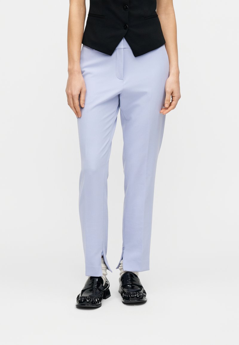 Ανοιχτό μπλε παντελόνι με στενή γραμμή, με φερμουάρ στο εμπρόσθιο μέρος των μανσετών και ομαλή, υφή με υφή. Φορεμένο με μαύρο γιλέκο και λαμπερά παπούτσια.
