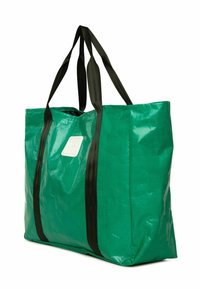 Zaļš polietilēna somas maisiņš ar melnām neilona siksnām, taisnstūra forma, spīdīga tekstūra un mazs balts logo sānos.