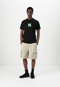 Black t-shirt with floral embroidery on the chest, beige cargo shorts, black socks, and black sneakers. Simple, relaxed fit.