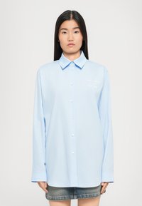 Camicia azzurra a maniche lunghe con colletto a punta, caratterizzata da un sottile dettaglio ricamato sul petto e polsini arrotondati.