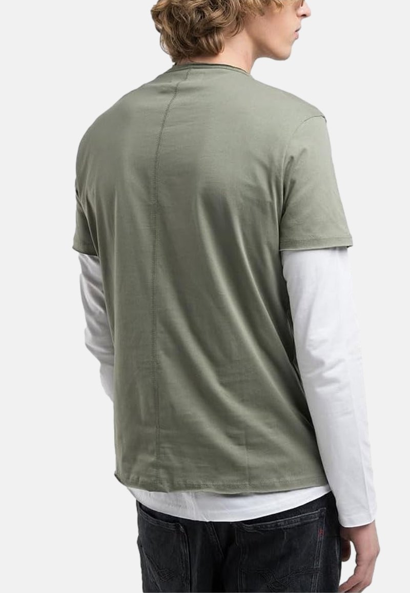 T-shirt olive green à manches courtes superposé sur une chemise blanche à manches longues, avec un col rond et des détails de couture visibles.