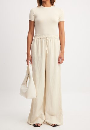 Beige fitted t-shirt paired with loose, light beige wide-leg trousers and a matching handbag. Smooth texture, neutral color palette.