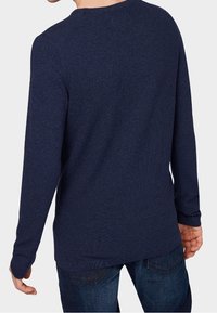 Pull bleu marine à manches longues avec une finition texturée, col rond et ourlet côtelé, porté sur un jean, vue de dos.