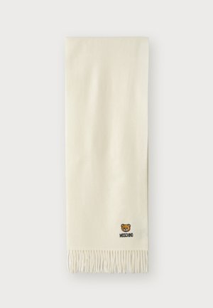 Bufanda color crema hecha de material suave, con bordes de flecos y un pequeño logotipo de oso bordado con el texto "Moschino".