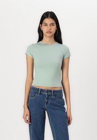 Tricou mint verde, ajustat, cu mâneci scurte, gât rotund și textură netedă, asortat cu blugi albaștri din denim cu talie înaltă.