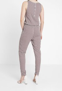 Mönstrad jumpsuit i röd och vit, med ärmlös design, åtsmitande midja och avsmalnade ben. Kompletteras med vita högklackade skor.