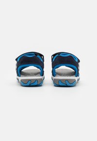 Sandalias azules y marinas con un upper texturizado, parte trasera abierta y correa ajustable. Presenta una suela de goma gris con tacos en forma de ola.