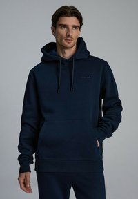 Granatowy sweatshirt z kapturem wykonany z miękkiego materiału, posiadający kieszeń z przodu i sznurki do regulacji. Minimalistyczne logo w subtelnym wzorze.