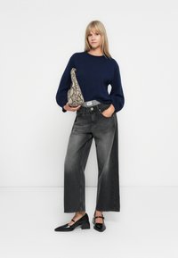 Marine gebreide trui, zwarte hoge taille wijde jeans, zwarte blokhak schoenen en een grijze tas met slangenpatroon. Minimalistisch ontwerp.