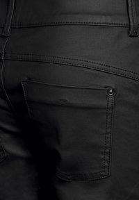 Mustat farkut, joissa on pieni takatasku napilla, tasosaumat, sileä pinta ja tyylikäs muotoilu ilman koristeluja.