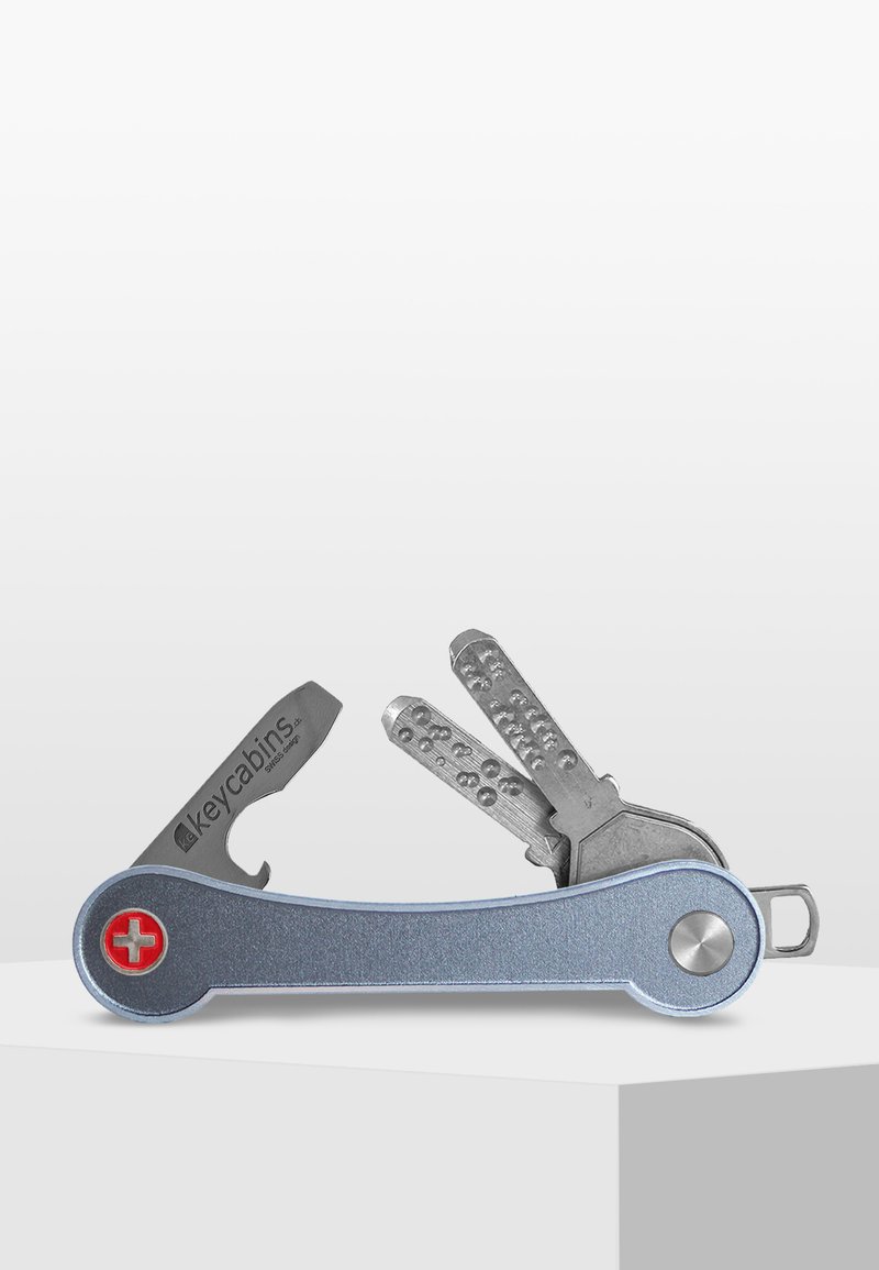 Multi-tool key holder with a blue aluminum body, silver metal tools, and a red cross logo. Features several angular keys and a flat edge design.