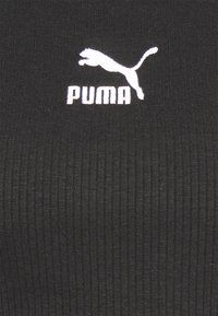 Logo Puma blanc avec un chat sautant et texte sur un fond en tissu côtelé noir.