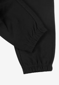 Czarne spodnie dresowe z elastycznymi mankietami, charakteryzujące się gładką teksturą i subtelnymi szwami, zaprojektowane z myślą o komforcie i swobodzie ruchów.