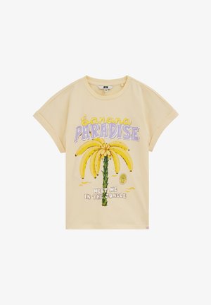 T-shirt beige à manches courtes avec manches retroussées présentant un graphisme de régimes de bananes en forme de palmier et le texte « banana paradise » et « meet me in the jungle ».