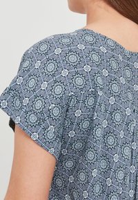 Haut à manches courtes avec un motif floral bleu, blanc et vert orné de dessins circulaires, fabriqué en tissu léger.