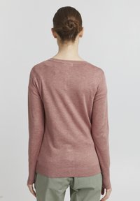 Pulover s dolgimi rokavi v svetlo roza barvi, izdelan iz mehkega pletenega materiala. Ima okroglo ovratnico in rebraste manšete. Preprost, oprijet dizajn.