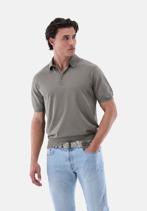 Graues Poloshirt mit kurzen Ärmeln, Kragen, zwei Knopfverschluss und geripptem Saum. Getragen mit hellblauen Jeans und einem gemusterten Gürtel.