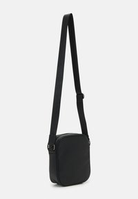 Black crossbody bag made of smooth material, featuring a square shape, adjustable strap, and minimalistic design. No visible patterns or hardware.