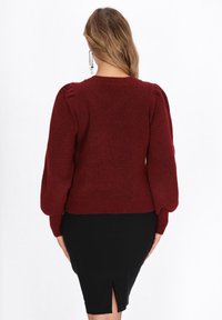 Roter strukturierter Pullover mit Puffärmeln und geripptem Saum, kombiniert mit einem schwarzen Rock mit Schlitz hinten. Eine einfache und figurbetonte Silhouette.