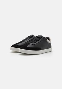 Svarte læringssneakers med semsket detaljer, lavprofil design, rund tå og hvit gummisåle. Har svarte snører og grå krage.