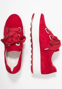 Baskets en daim rouge avec une semelle en caoutchouc blanche texturée, dotées de lacets ronds et d'un design de nœud distinctif sur la languette.