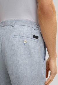 Jasnoniebieskie spodnie w wzory o teksturowanym wykończeniu, z tylną kieszenią na guzik i akcentem w postaci czarnej metki.