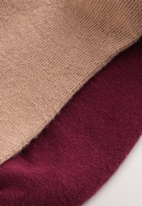 Gebreide stof in beige en bordeaux, met een gladde textuur. De twee kleuren zijn gelaagd, met duidelijke stiksels en randen.