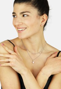 Layered silver necklaces with small pearl and gemstone accents, matching earrings, and rings displayed on a model's hands and shoulders.