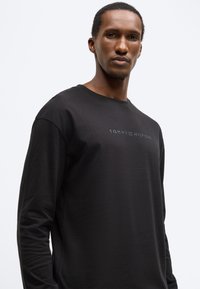 Czarna bawełniana koszulka z długim rękawem. Posiada okrągły dekolt oraz subtelne, ciemne logo TOMMY HILFIGER na piersi.