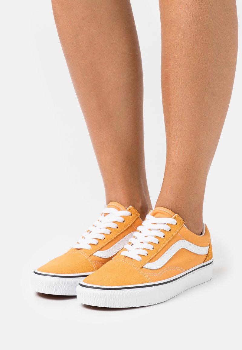 Orange suede sneakers with white accents, featuring a low-top design, white laces, a rounded toe, and a rubber sole with a black stripe.