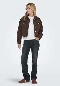 Chaqueta corta de piel de leopardo marrón con botones de presión plateados, llevada sobre una camisa blanca, combinada con jeans oscuros y zapatillas burdeos.