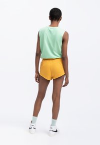 Haut sans manches vert menthe associé à un short jaune vif. Le short comporte des poches latérales et un ourlet arrondi. Complété avec des baskets blanches.