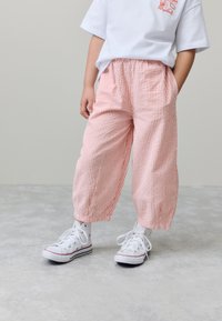 Pantaloni a gamba larga a strisce rosa e bianche con vita elastica. Indossati con sneakers bianche. Tessuto liscio, design casual, tasche laterali.
