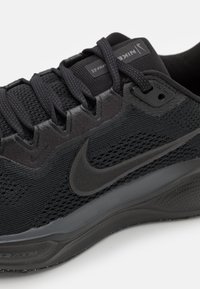 Chaussure de sport noire avec un dessus en mesh, des superpositions synthétiques, des lacets texturés et une semelle rembourrée arborant un logo Nike bien visible.