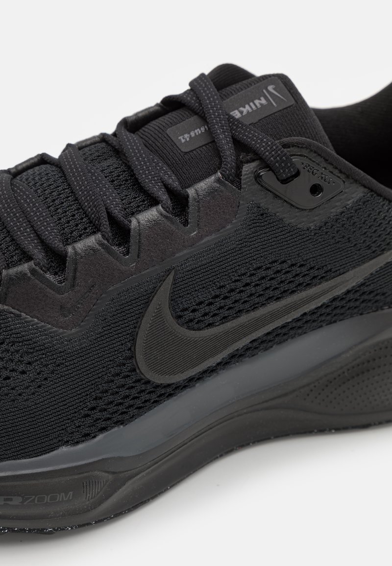 Zapatilla deportiva negra con parte superior de malla, superposiciones sintéticas, cordones texturizados y una suela acolchada que presenta un destacado logo de Nike.