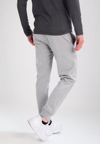 Gray sweatpants with a slim fit design, ribbed cuffs, and side pockets, paired with white athletic sneakers. Soft texture, casual style.