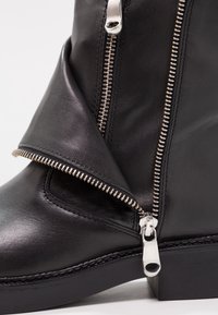 Czarne skórzane botki sięgające kostki z boku na zamek, odsłoniętymi szwami, załamanym klapą i masywną czarną podeszwą. Błyszcząca faktura z metalowymi akcentami.