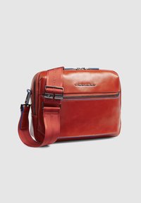 Borsa a tracolla in pelle rossa con compartimento principale con zip, tasca frontale e tracolla regolabile con dettagli blu e branding.