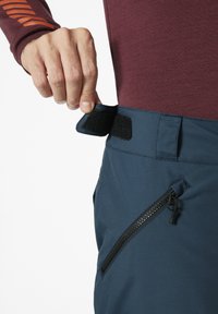 Blauwe outdoorbroek met een klittenbandsluiting bij de taille en een ritszak aan de zijkant, gemaakt van een gestructureerd, lichtgewicht materiaal.