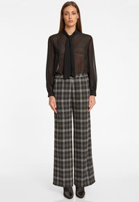 Zwarte transparante blouse met een strik rond de nek, gecombineerd met wijde zwarte en grijze geruite broek, met een zachte textuur en een op maat gemaakte silhouette.