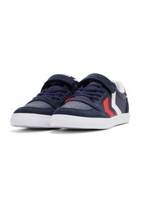 Blauwe leren sneakers met witte en rode accenten, ronde neus, vetersluiting aan de voorkant met klittenbandsluiting, witte rubberen zool en geperforeerde details.
